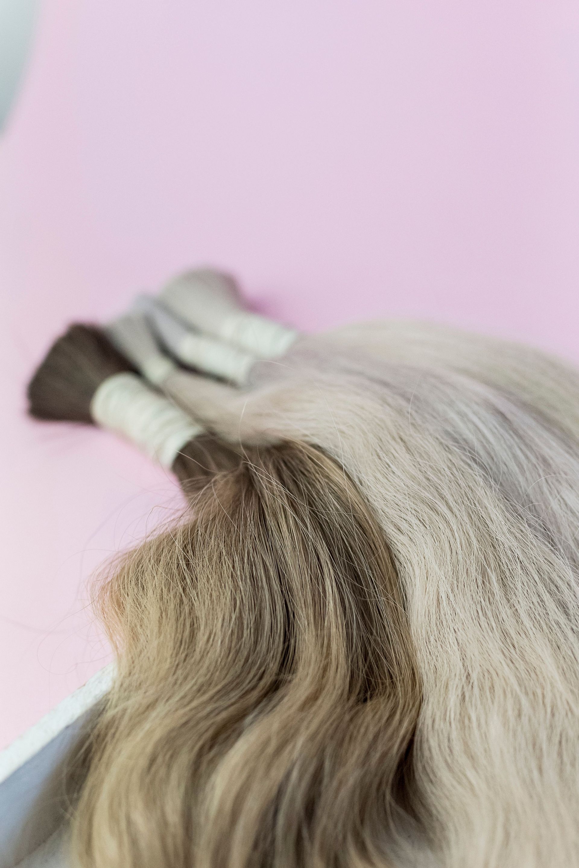 Close-up of blonde hair extensions against a light pink background.